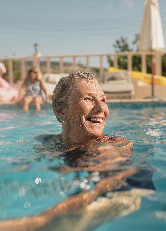 senior woman looks off into the distance and smiles while swimming in an outdoor pool