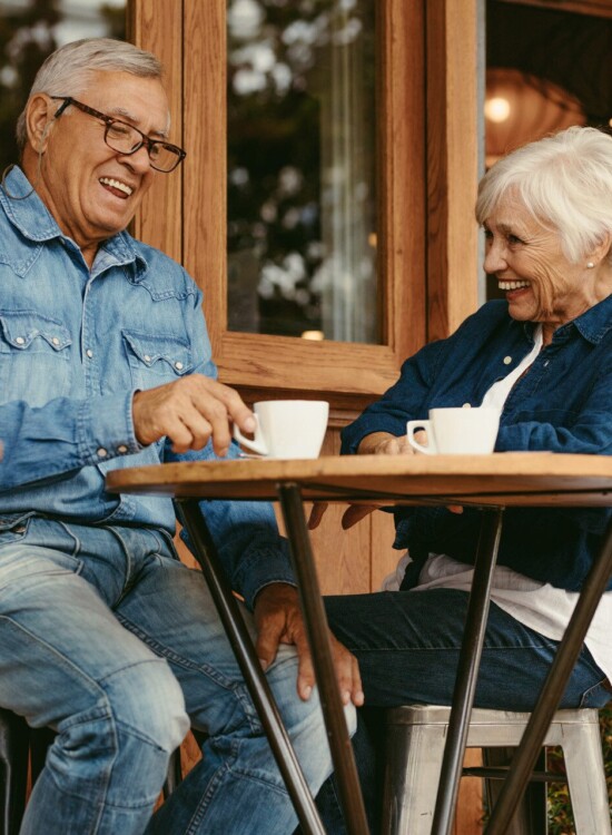 senior couple sits at small outdoor cafe table enjoying coffee