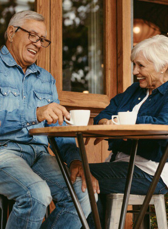 senior couple sits at small outdoor cafe table enjoying coffee