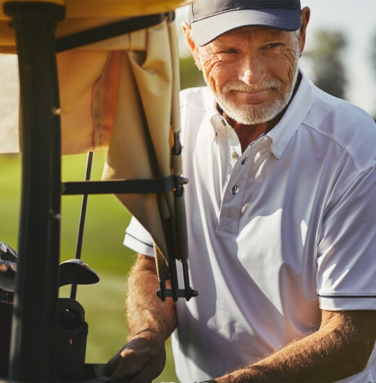 senior man smiles while loading golf clubs after a game
