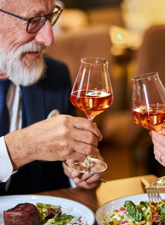 senior couple toasts glasses of wine together over an elegant, upscale meal