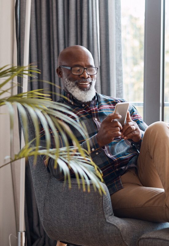 senior man relaxes on chair with his feet up, scrolling through his phone