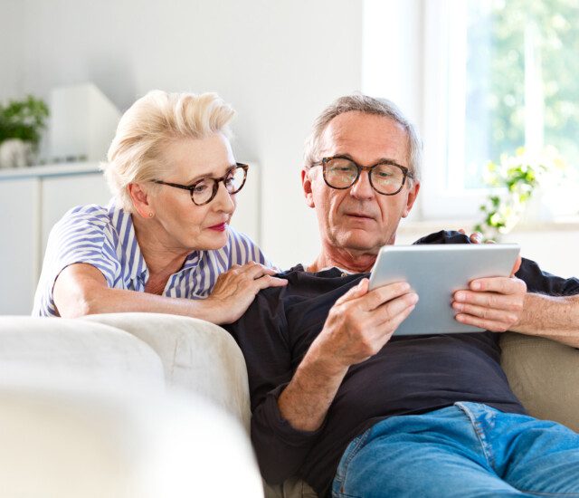senior couple relaxing at home while looking at a tablet in the senior man's hands