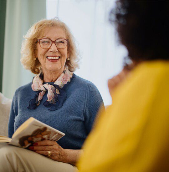 senior woman smiles while reading book and conversing with friend