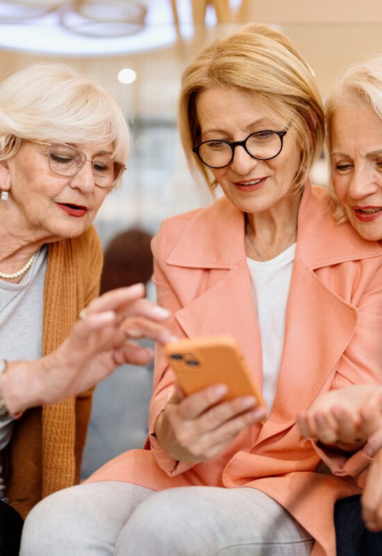 group of senior women smile and browse through a phone together while seated