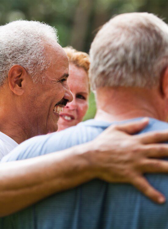 senior man with arm around another man's shoulder, smiling