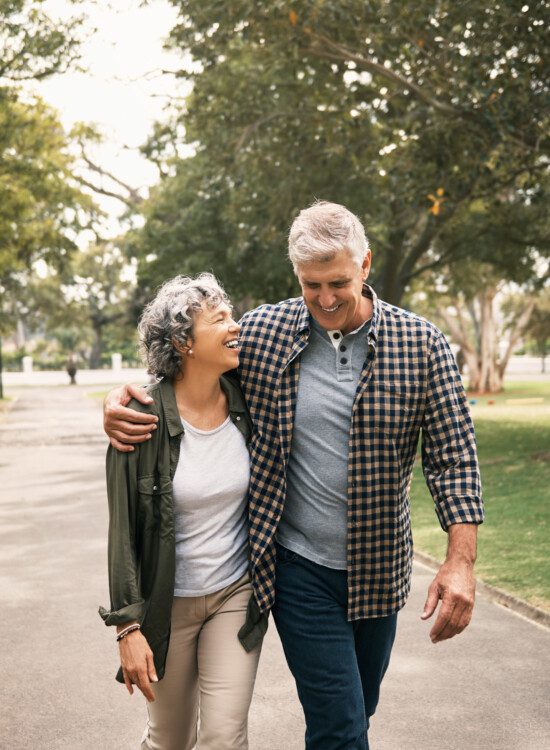 senior couple smiles and laughs together while walking arm-in-arm on a scenic path outdoors