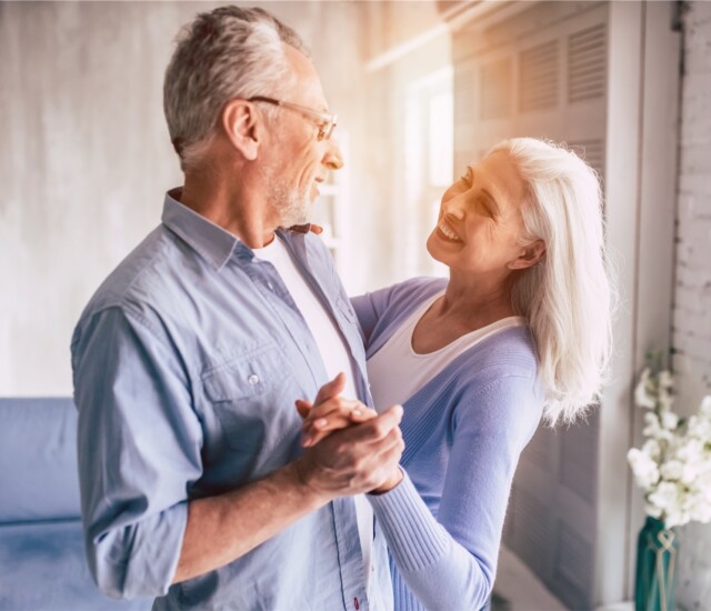 senior couple dances in their apartment, backdropped by sunlight