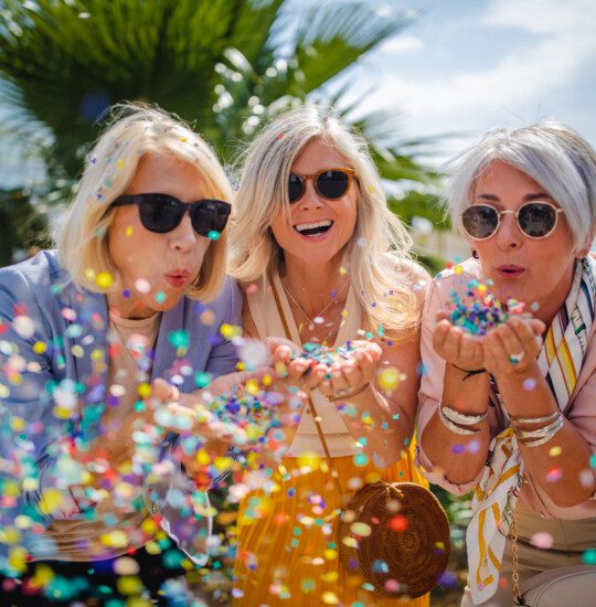 Fashionable senior friends having fun and celebrating by blowing colorful confetti in city street