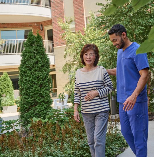 senior woman walks with caregiver outside on a scenic walking path