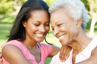 senior woman and her adult daughter smile and embrace outdoors