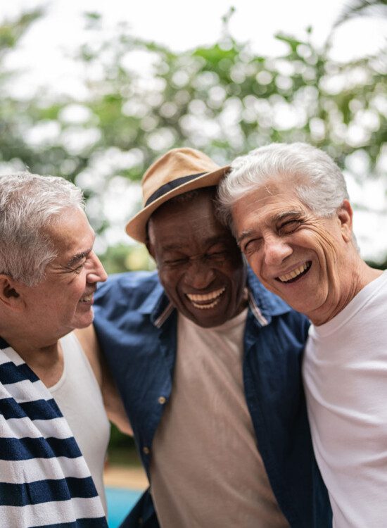 group of three senior men smile and hug outside