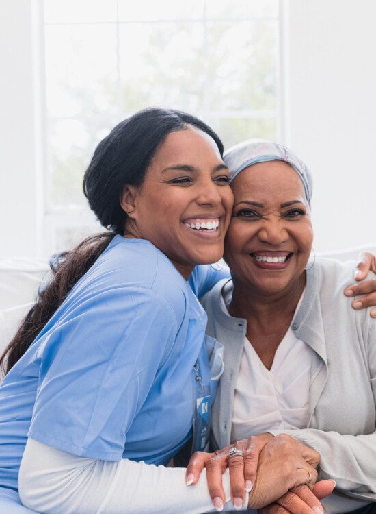 seated senior woman and caregiver hug on couch, smiling