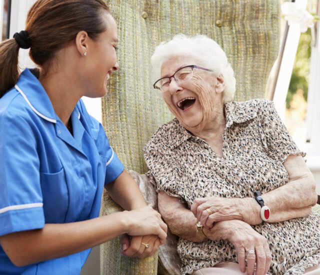 seated senior woman laughs and smiles at her care giver outdoors