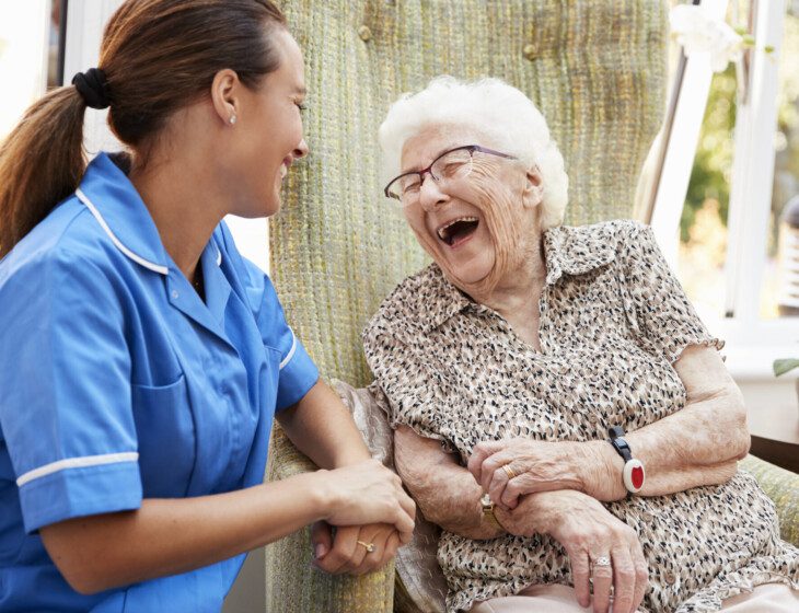 seated senior woman laughs and smiles at her care giver outdoors