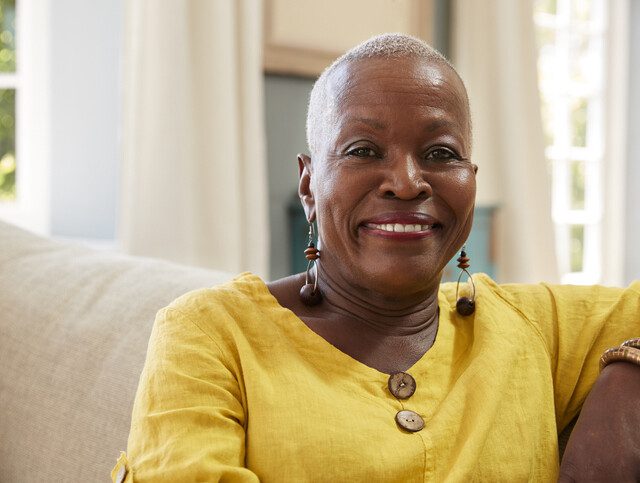 Happy senior woman smiles confidently at the camera while seated on a couch inside of her home