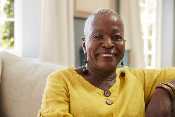 Happy senior woman smiles confidently at the camera while seated on a couch inside of her home