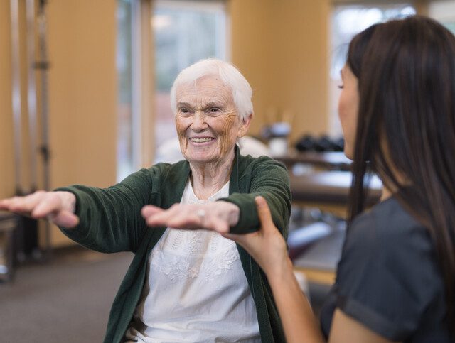 seated senior woman performs physical therapy exercise with the help of her trainer
