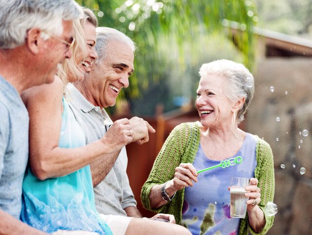 group of senior friends laugh and blow bubbles outdoors