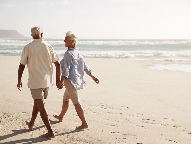 senior couple in casual clothing holds hands and walks along the beach