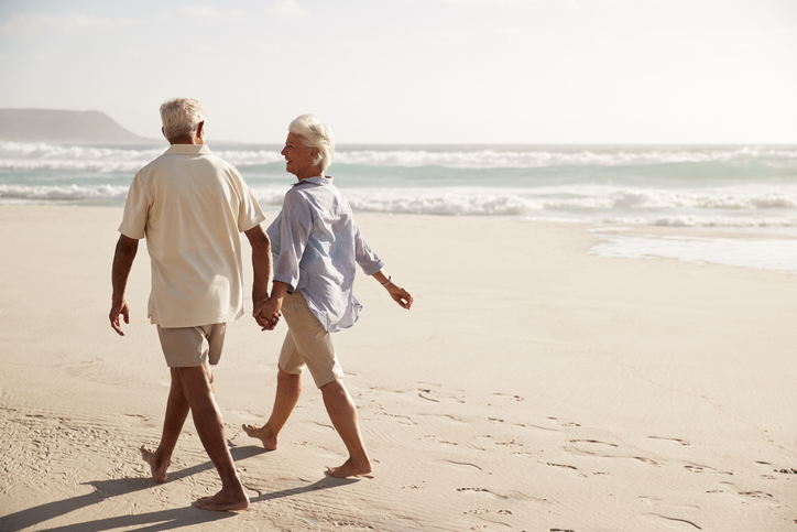 senior couple in casual clothing holds hands and walks along the beach