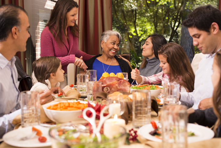 senior woman seated at the head a table smiles and shares a Thanksgiving meal with family