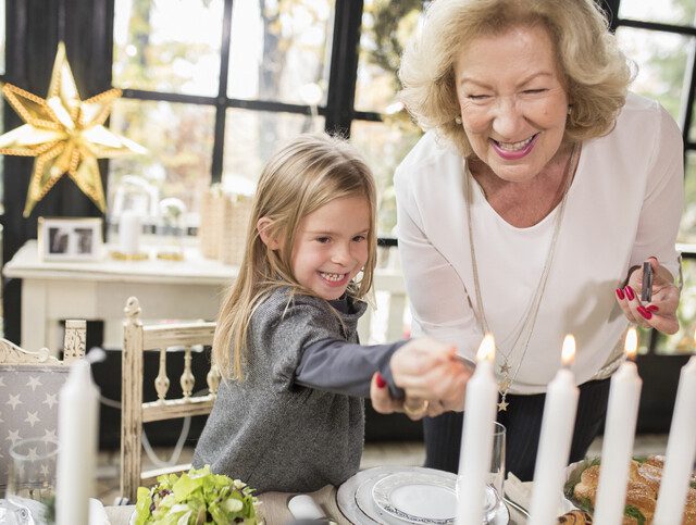 senior woman and her granddaughter smile and light candles on the table for a holiday celebration