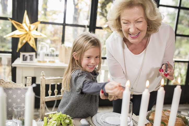 senior woman and her granddaughter smile and light candles on the table for a holiday celebration