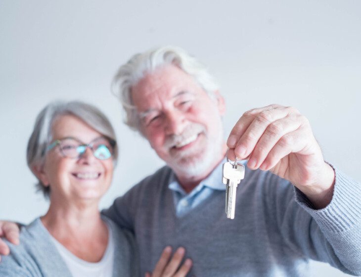 smiling senior couple holds out the keys to their new apartment