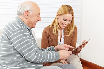 senior man and his adult daughter smile and look at an old photo together while seated