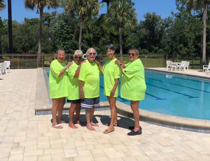 senior residents in matching green shirts stand in front of a resort-style swimming pool at Village on the Green