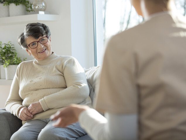 senior woman sitting on sofa talking to caregiver with back to audience