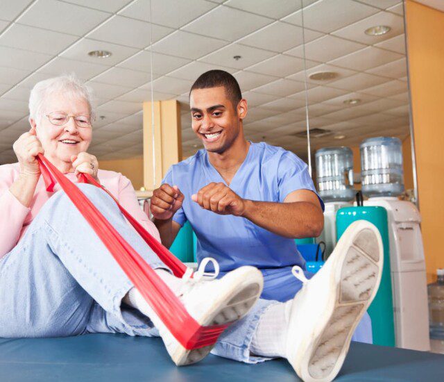 senior woman uses resistance band to complete physical therapy exercise as her trainer excitedly encourages her