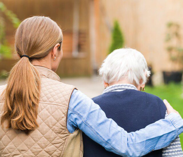 senior man walks away from the camera with his adult daughter, whose arm is around his shoulder