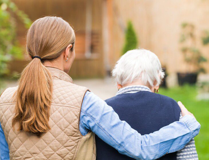 senior man walks away from the camera with his adult daughter, whose arm is around his shoulder