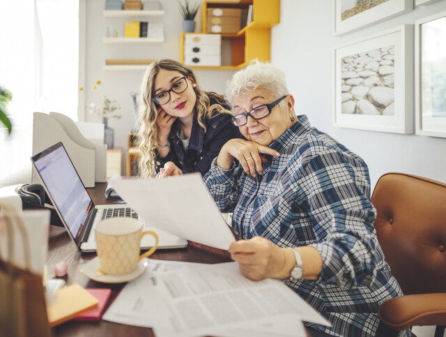 senior woman and her adult daughter examine papers while seated in front of a laptop