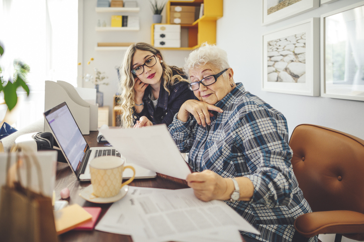 senior woman and her adult daughter examine papers while seated in front of a laptop