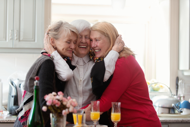 group of three senior women with mimosas smile and embrace