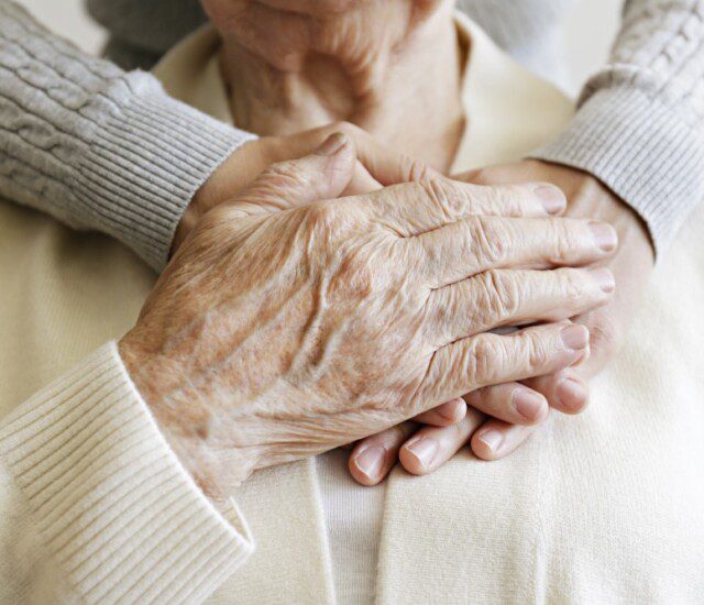 close-up of senior with their adult child embracing them from behind, arms around the neck