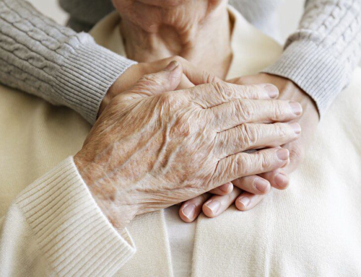 close-up of senior with their adult child embracing them from behind, arms around the neck