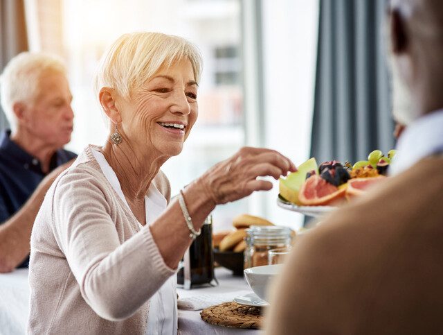 senior woman selects fruit from a plate while smiling at a social event