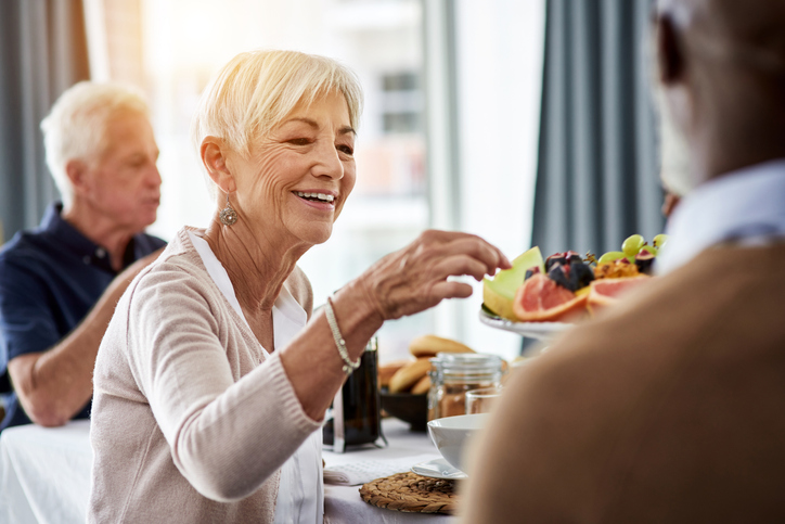 senior woman selects fruit from a plate while smiling at a social event