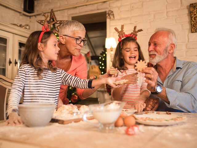 senior couple and their twin granddaughters smile while baking cookies for the holidays