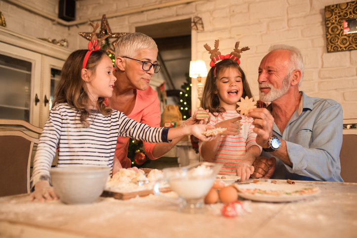 senior couple and their twin granddaughters smile while baking cookies for the holidays