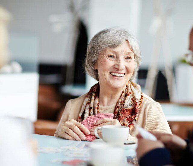 senior woman smiles at her companions while playing a game of cards