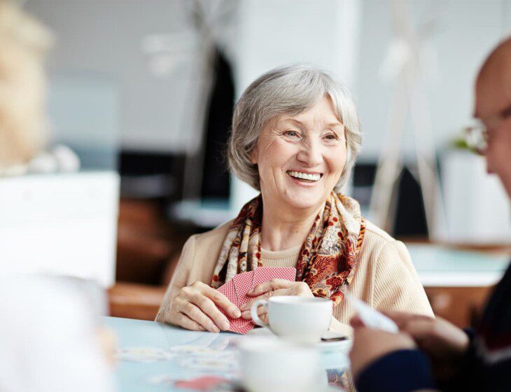 senior woman smiles at her companions while playing a game of cards