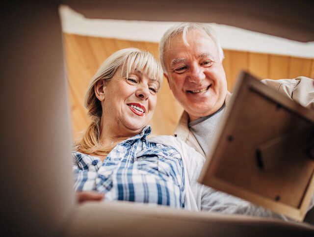 smiling senior couple examine an old photograph while packing a box for a move