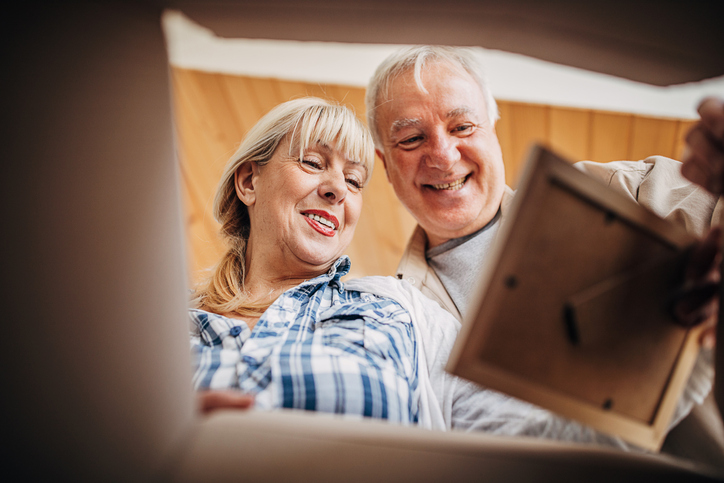 smiling senior couple examine an old photograph while packing a box for a move