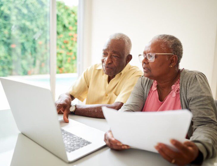 senior couple sit at a table and look at a laptop screen and documents together