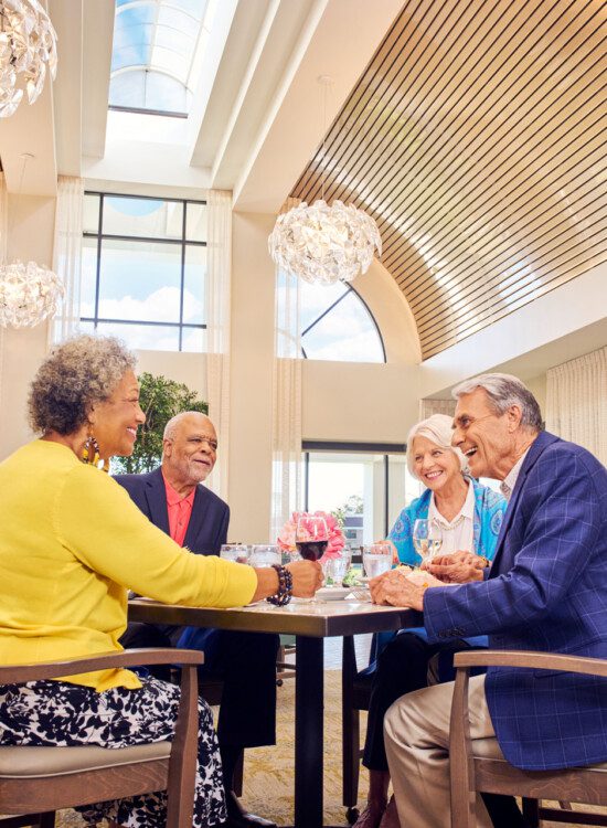 group of senior friends smile and enjoy an elegant dinner together at Village on the Green Senior Living Community